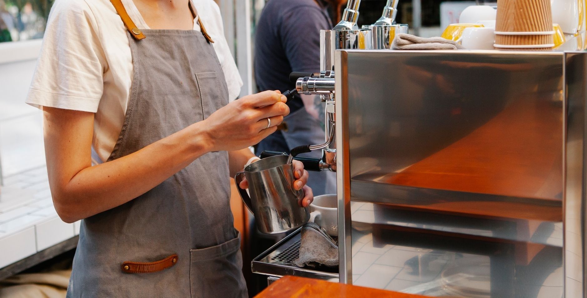 Barista operates an espresso machine beside a stainless-steel milk pitcher